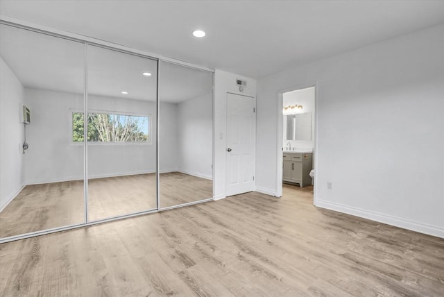 unfurnished bedroom with sink, ensuite bath, a closet, and light wood-type flooring