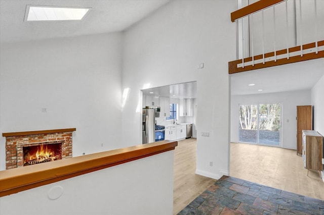 corridor featuring sink, a towering ceiling, a skylight, and light wood-type flooring