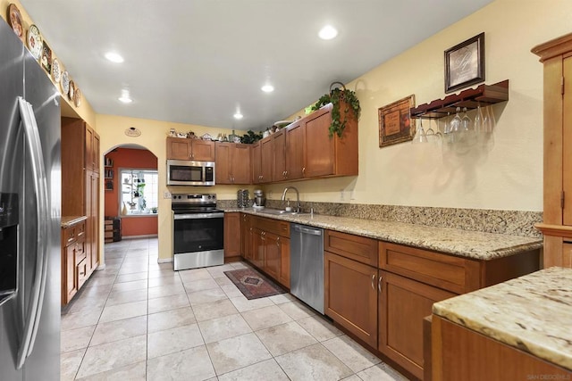 kitchen featuring light stone counters, sink, light tile patterned floors, and appliances with stainless steel finishes