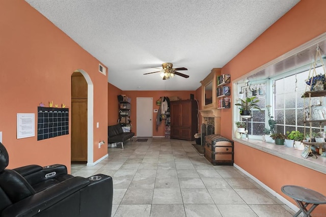 living room featuring ceiling fan, a fireplace, a textured ceiling, and light tile patterned floors