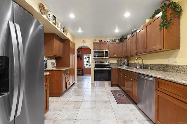 kitchen featuring appliances with stainless steel finishes, sink, light tile patterned floors, and light stone counters