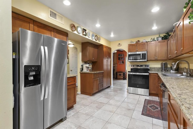 kitchen with stainless steel appliances, light stone countertops, sink, and light tile patterned floors