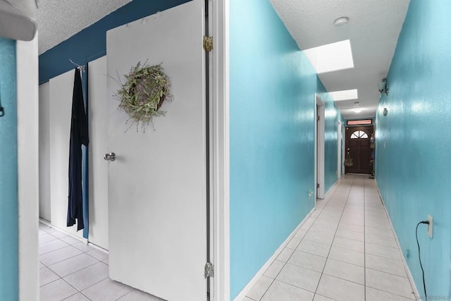 hall featuring light tile patterned flooring, a skylight, and a textured ceiling