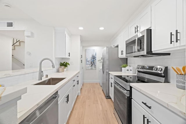 kitchen with stainless steel appliances, white cabinetry, sink, and light stone counters