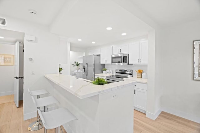 kitchen featuring white cabinetry, light hardwood / wood-style flooring, a kitchen breakfast bar, kitchen peninsula, and stainless steel appliances