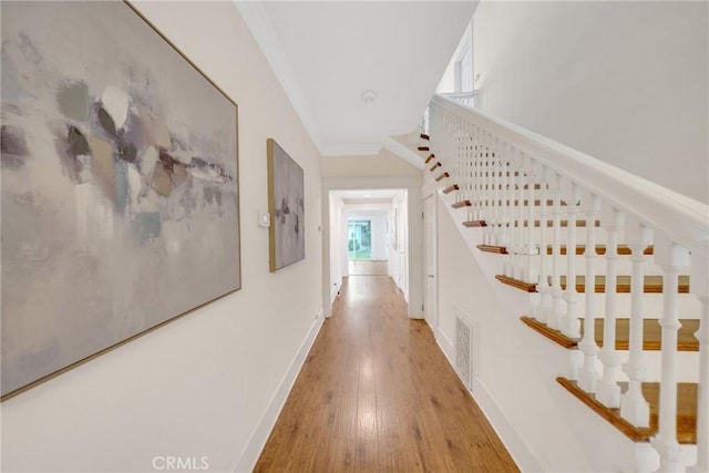 hallway featuring visible vents, baseboards, crown molding, light wood finished floors, and stairway