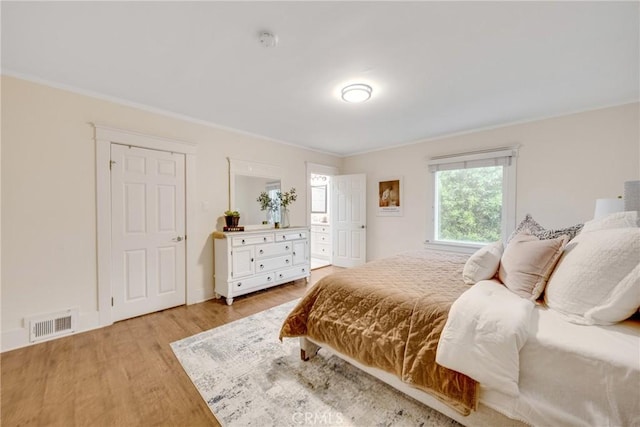 bedroom with crown molding, visible vents, and light wood finished floors