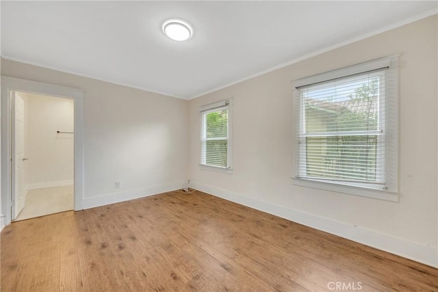 spare room featuring baseboards, light wood-type flooring, and ornamental molding