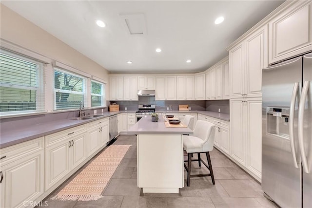 kitchen featuring a sink, appliances with stainless steel finishes, a breakfast bar, under cabinet range hood, and a kitchen island