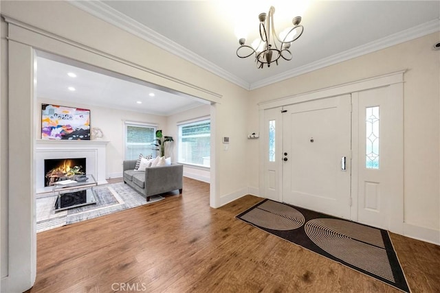 foyer entrance with a lit fireplace, ornamental molding, a chandelier, wood finished floors, and baseboards
