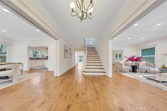 entrance foyer featuring light wood-style floors, crown molding, a notable chandelier, and stairway