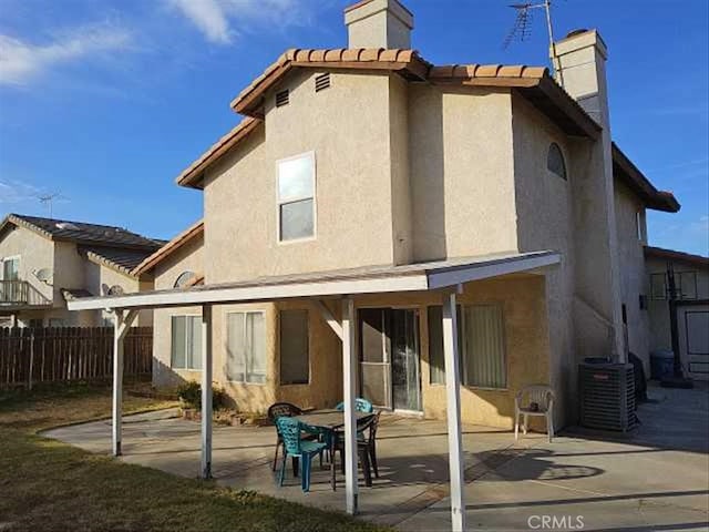 rear view of house featuring central air condition unit, fence, stucco siding, a chimney, and a patio area