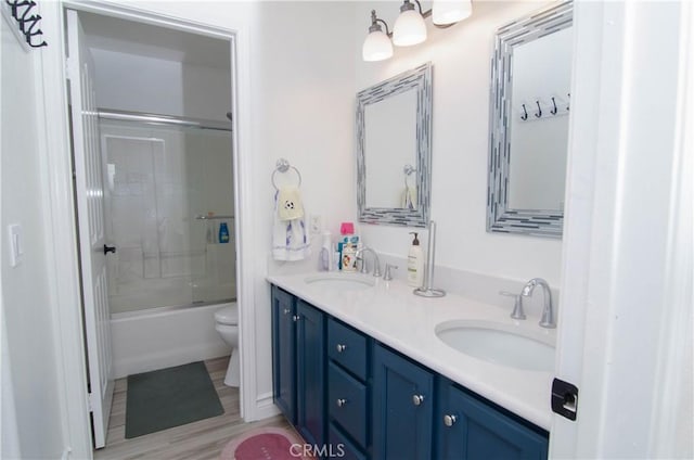 full bathroom featuring wood-type flooring, bath / shower combo with glass door, vanity, and toilet