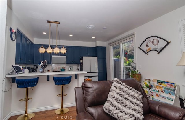 kitchen featuring blue cabinetry, a kitchen breakfast bar, dark wood-type flooring, stainless steel fridge, and kitchen peninsula