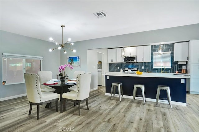 dining room with an inviting chandelier, sink, and light hardwood / wood-style floors