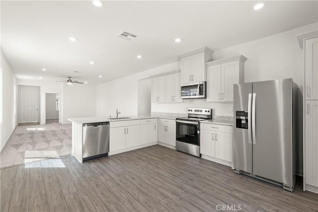 kitchen featuring sink, kitchen peninsula, stainless steel appliances, hardwood / wood-style floors, and white cabinets