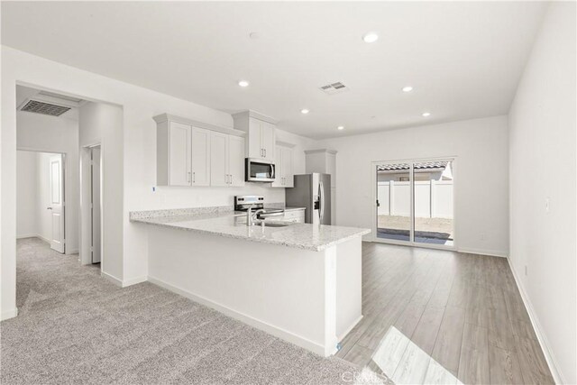 kitchen with sink, light stone counters, kitchen peninsula, stainless steel appliances, and white cabinets