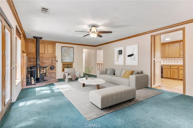 living room with visible vents, ceiling fan, ornamental molding, a wood stove, and carpet