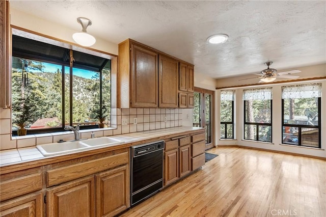 kitchen featuring tile countertops, a sink, brown cabinetry, and dishwasher