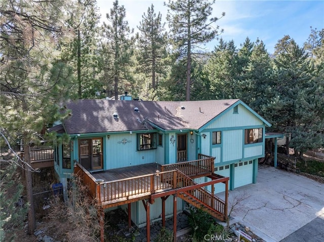 rear view of property featuring stairs, driveway, roof with shingles, and an attached garage