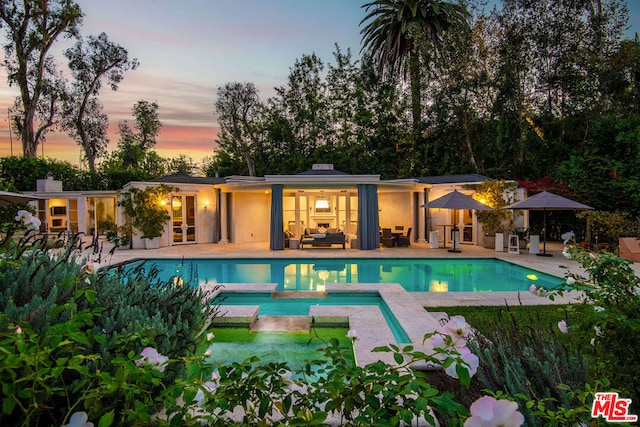 pool at dusk featuring an in ground hot tub, outdoor lounge area, and a patio