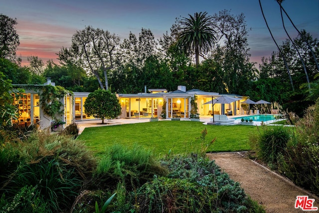 back house at dusk featuring a yard and a patio area