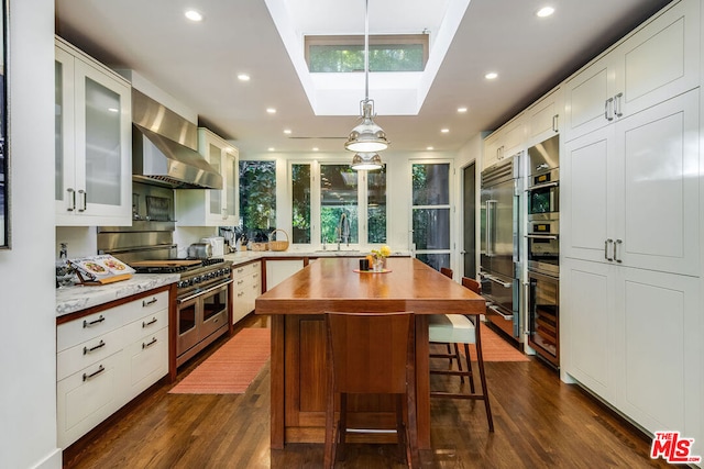 kitchen with wall chimney range hood, white cabinetry, hanging light fixtures, a center island, and high end appliances