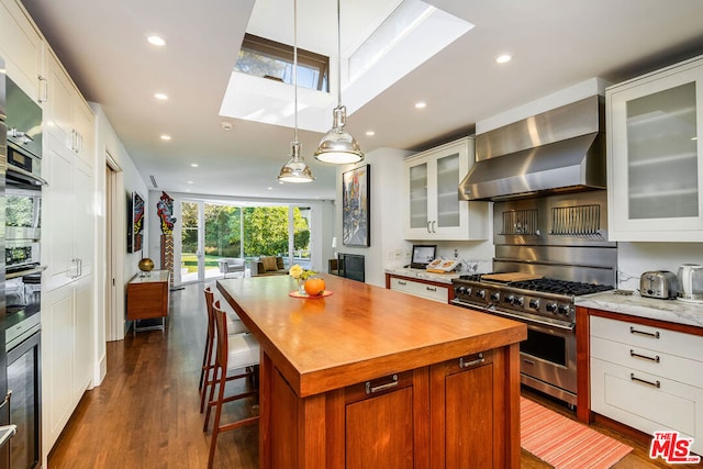 kitchen with wall chimney range hood, appliances with stainless steel finishes, white cabinetry, hanging light fixtures, and a center island