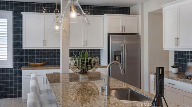 kitchen featuring white cabinetry, sink, hanging light fixtures, light stone counters, and stainless steel refrigerator with ice dispenser