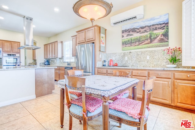 kitchen featuring light tile patterned floors, appliances with stainless steel finishes, light stone counters, island exhaust hood, and an AC wall unit