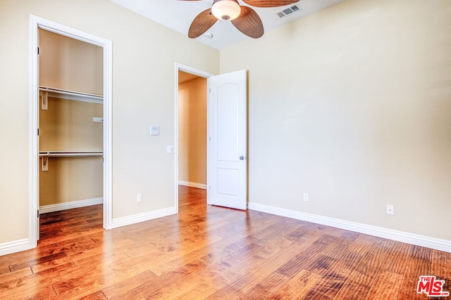 unfurnished bedroom with a spacious closet, light hardwood / wood-style flooring, a closet, and ceiling fan