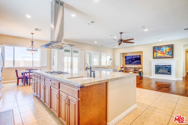 kitchen featuring sink, a kitchen island with sink, island range hood, light stone countertops, and light tile patterned flooring