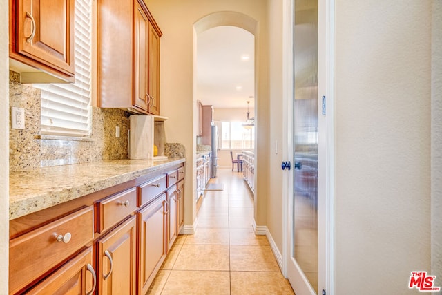 kitchen with tasteful backsplash, light tile patterned floors, light stone countertops, and stainless steel refrigerator