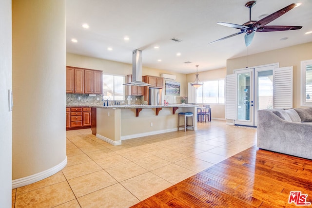 kitchen with a kitchen island, a breakfast bar, stainless steel refrigerator, decorative backsplash, and island exhaust hood