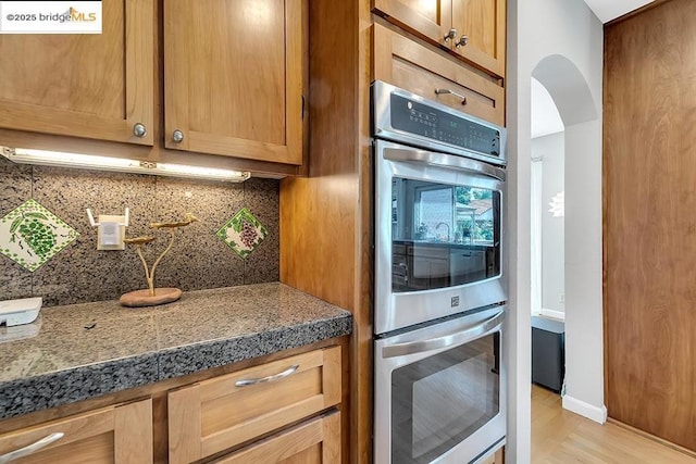 kitchen with tasteful backsplash, light hardwood / wood-style flooring, and stainless steel double oven