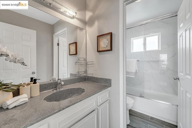 full bathroom featuring vanity, shower / bath combination with glass door, and toilet