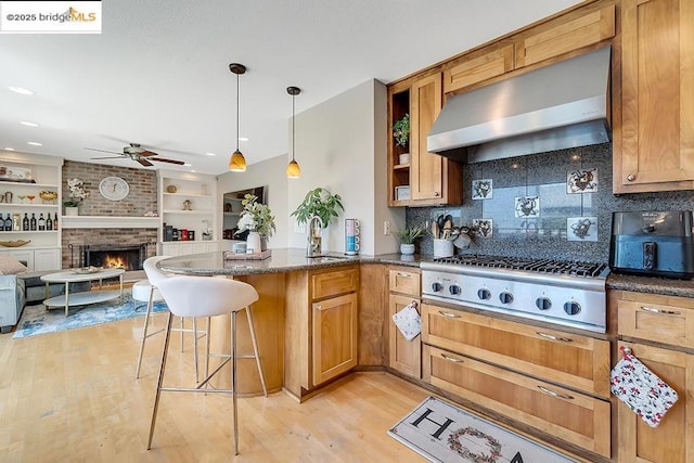 kitchen featuring stainless steel gas cooktop, ventilation hood, light hardwood / wood-style flooring, a kitchen breakfast bar, and kitchen peninsula