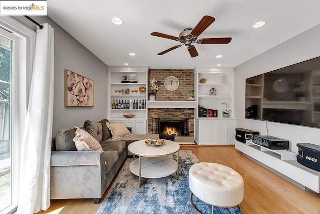 living room with built in shelves, a fireplace, light hardwood / wood-style floors, and ceiling fan