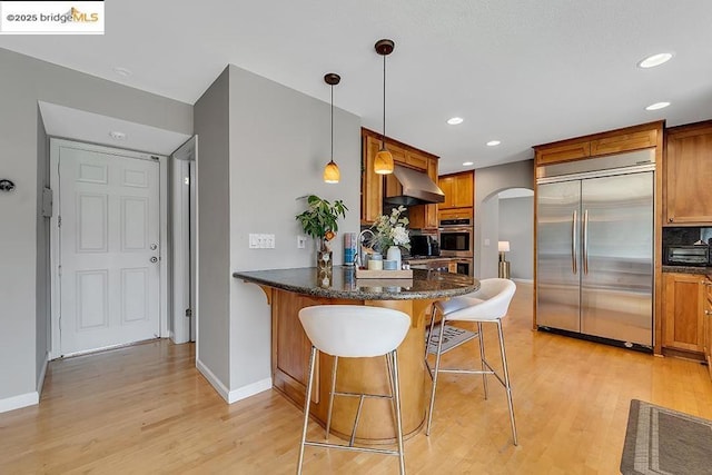 kitchen featuring extractor fan, appliances with stainless steel finishes, a kitchen bar, hanging light fixtures, and kitchen peninsula