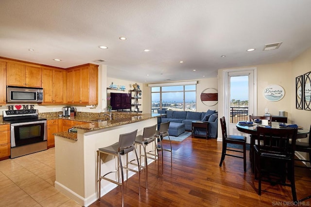 kitchen with sink, dark stone countertops, stainless steel appliances, a kitchen bar, and kitchen peninsula