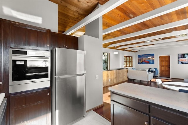 kitchen featuring beamed ceiling, dark brown cabinets, and stainless steel refrigerator