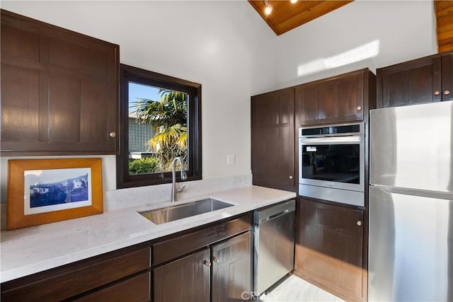 kitchen with dark brown cabinetry, sink, light stone counters, and appliances with stainless steel finishes