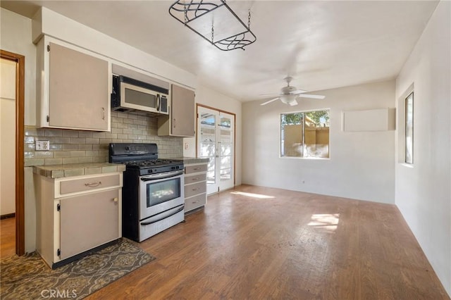 kitchen with tile countertops, backsplash, appliances with stainless steel finishes, light wood-style floors, and a ceiling fan