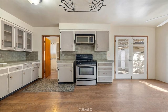 kitchen with light wood-type flooring, glass insert cabinets, stainless steel appliances, and light countertops