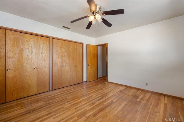 unfurnished bedroom with baseboards, visible vents, light wood finished floors, and two closets