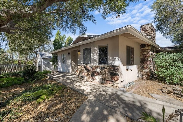 view of front of home featuring a chimney, fence, and stucco siding