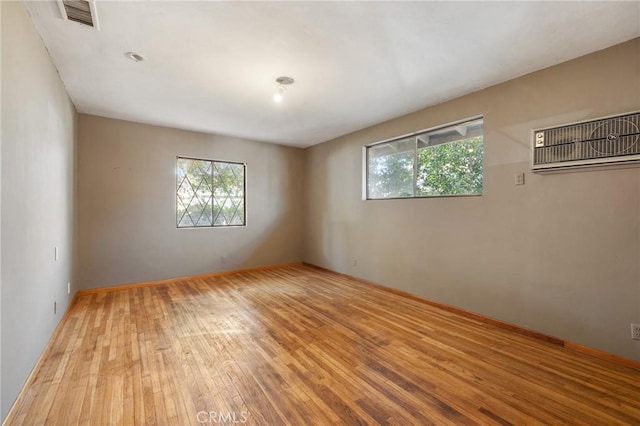 empty room featuring light wood-style floors, baseboards, visible vents, and an AC wall unit