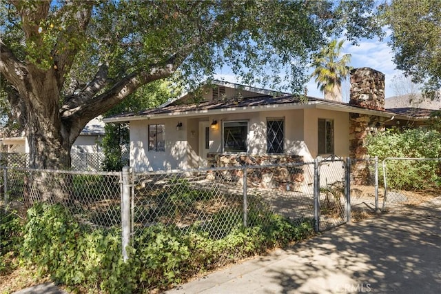 bungalow-style house with a fenced front yard, a gate, a chimney, and stucco siding