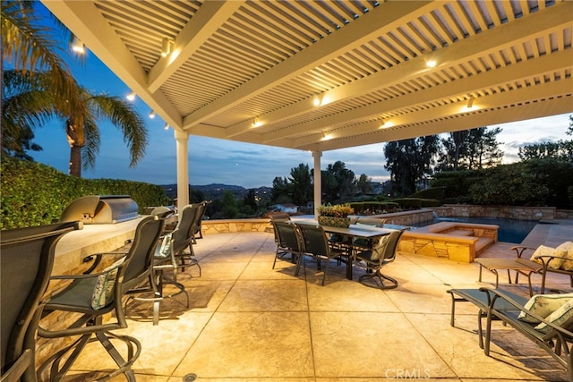 patio terrace at dusk with exterior kitchen and a pergola