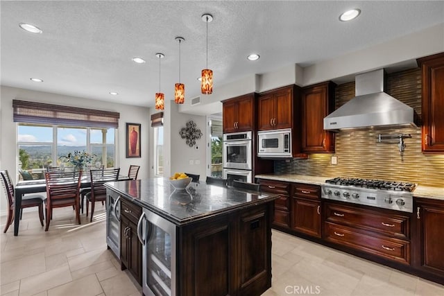 kitchen featuring wall chimney range hood, appliances with stainless steel finishes, wine cooler, a kitchen island, and decorative light fixtures